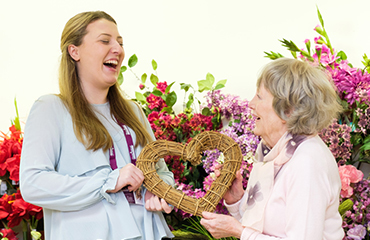 CAREGiver laughing with elderly lady holding a wooden heart