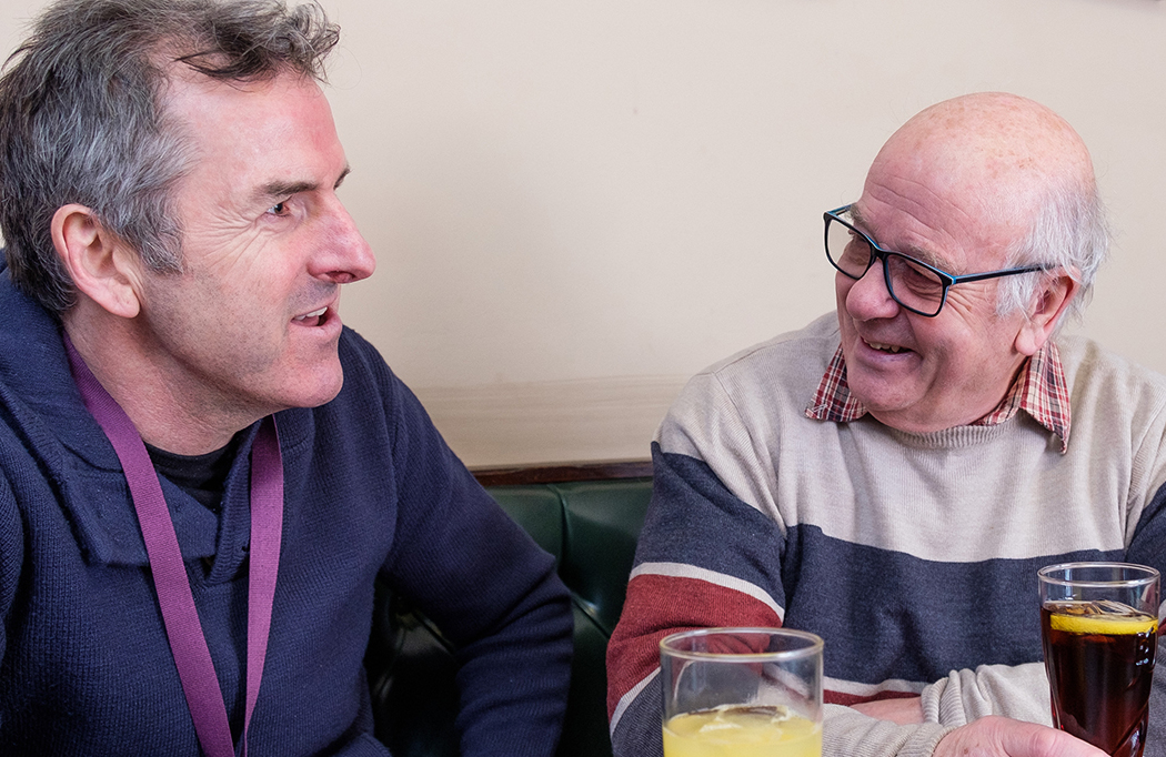 Male CAREGiver talking to an elderly male client over a drink in pub