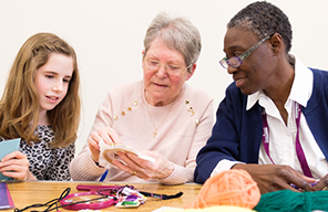 CareGiver crocheting with young girl and elderly lady