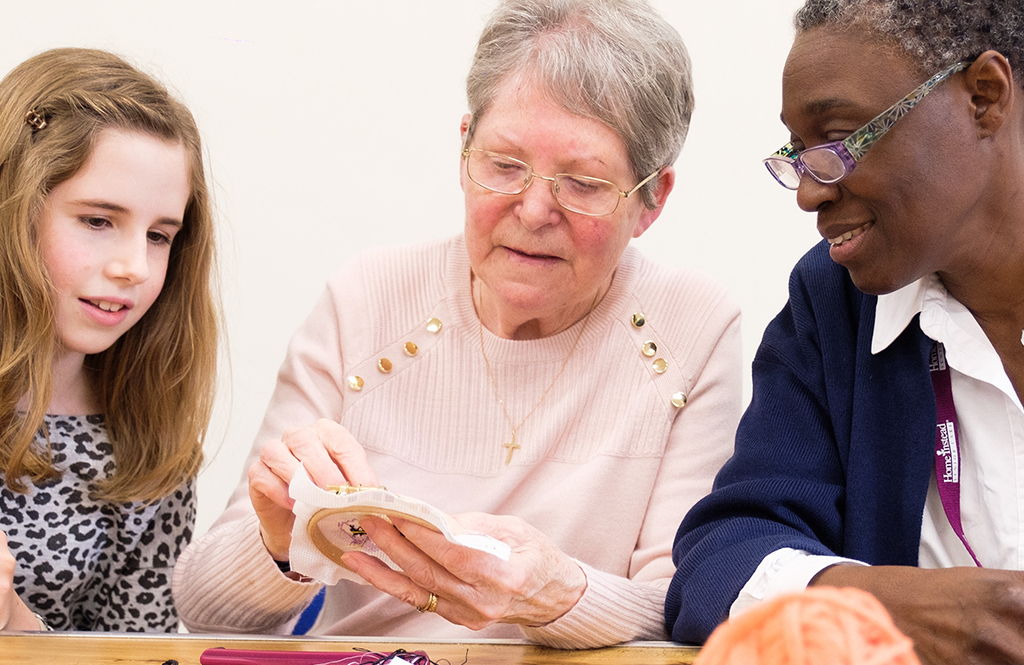 An elderly lady crocheting with a Home Instead CAREGiver