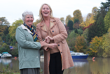 CAREGiver and elderly lady laughing whilst out on a walk by a lake
