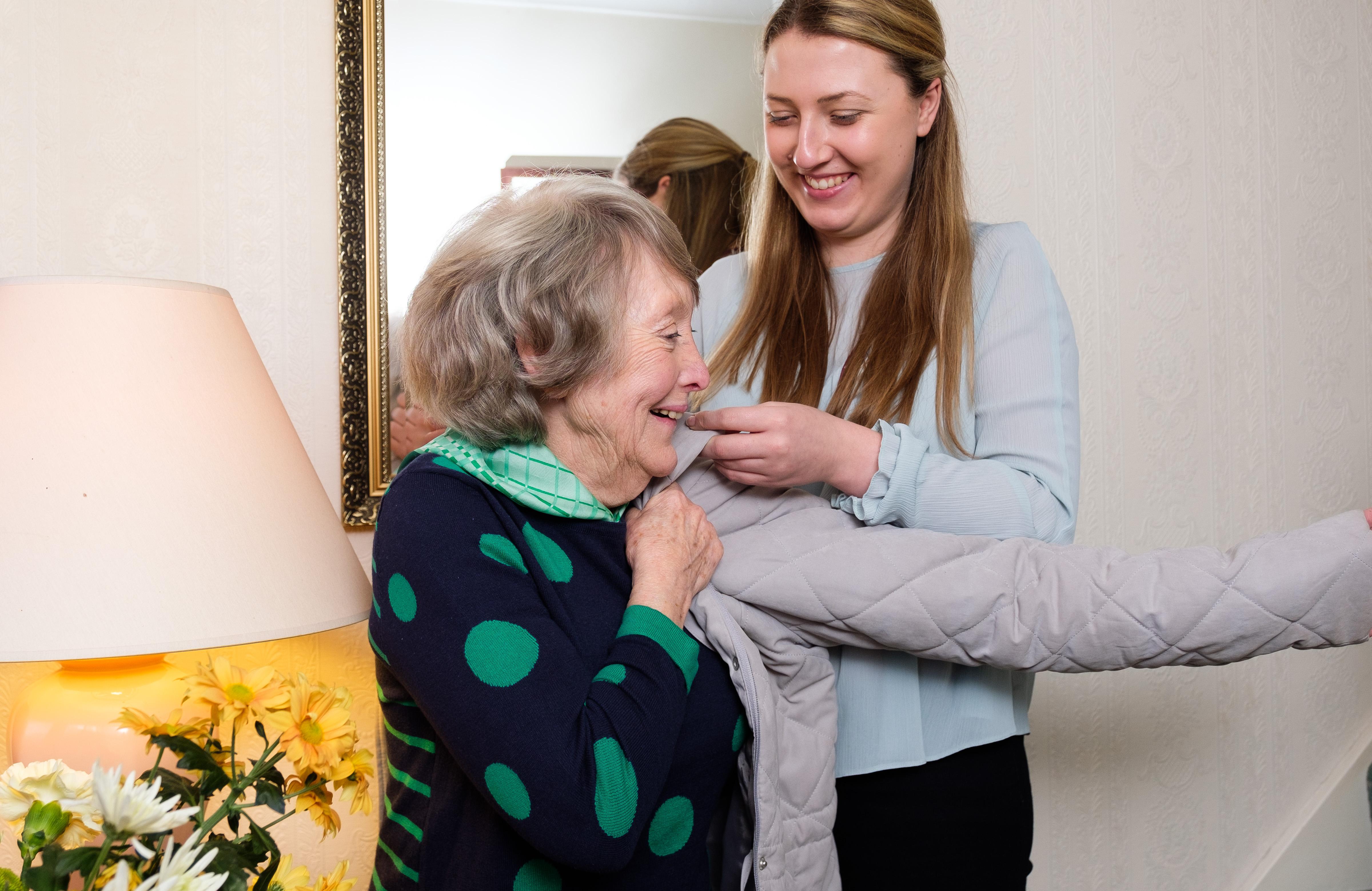 lady helped by caregiver coat on